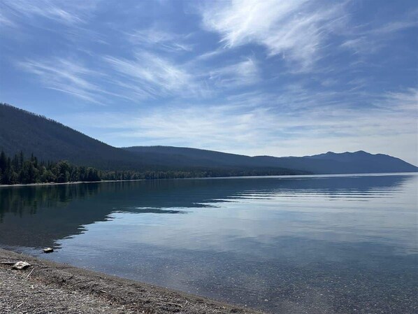Un lago tranquilo con una montaña boscosa al fondo.