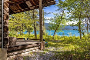 Une cabane en bois dotée d’une terrasse donnant sur un lac, entourée d’arbres et d’un paysage naturel.