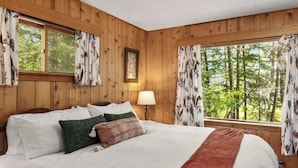 Een slaapkamer met houten lambrisering, een groot bed, een bedlampje en gordijnen.