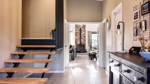 A modern interior with a wooden staircase, a kitchen area with a black countertop, and a brick wall in the background. - STYLISH AND SOPHISTICATED TWO STOREY RETREAT WITH SPARKLING POOL (Dunsborough)