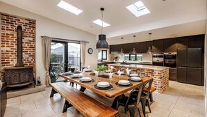 A modern kitchen with a central island, built-in appliances, and a dining area with a wooden table and benches. - STYLISH AND SOPHISTICATED TWO STOREY RETREAT WITH SPARKLING POOL (Dunsborough)