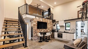 A modern kitchen with a brick accent wall, a dining area with two chairs, and a staircase with wooden steps. - STYLISH AND SOPHISTICATED TWO STOREY RETREAT WITH SPARKLING POOL (Dunsborough)