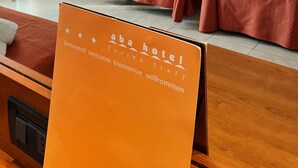 A hotel room with two beds, a wooden headboard, and a sign indicating the hotel name and location. - Hotel Aba (Moncalieri)