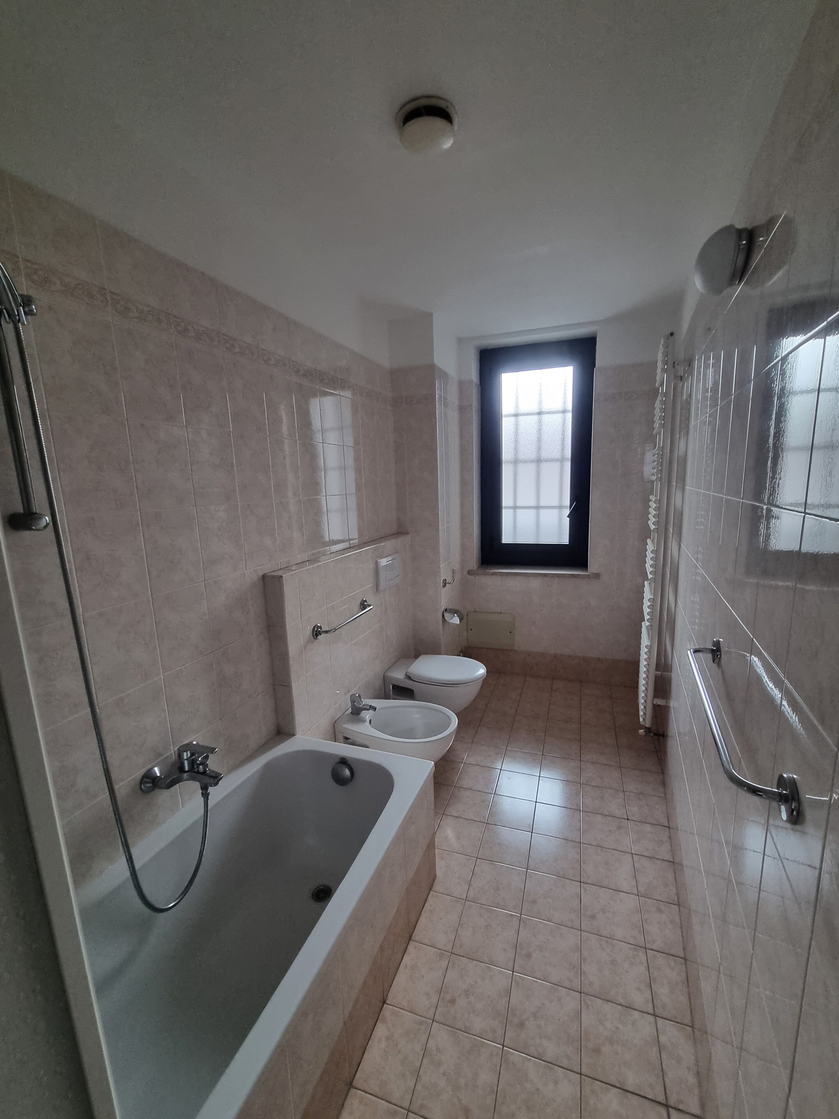 A bathroom with a bathtub, two toilets, a window, and a shower area.