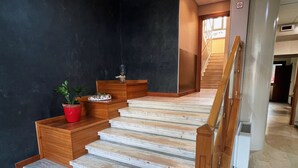 A modern staircase with wooden steps and a handrail, leading to a landing with a dark wall and a potted plant. - Hotel Aba (Moncalieri)