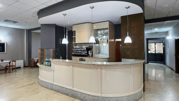 A modern bar area with a curved counter, pendant lighting, and a coffee machine. - Hotel Aba (Moncalieri)