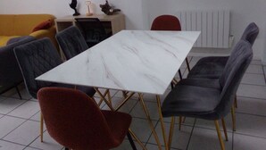 A dining area with a white marble table, red and gray upholstered chairs, a yellow sofa, and a wall-mounted artwork.