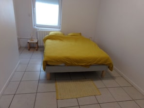 A bedroom with a bed, a small bedside table, a window, and a patterned rug. - Bright and comfortable, with garden (Valenciennes)