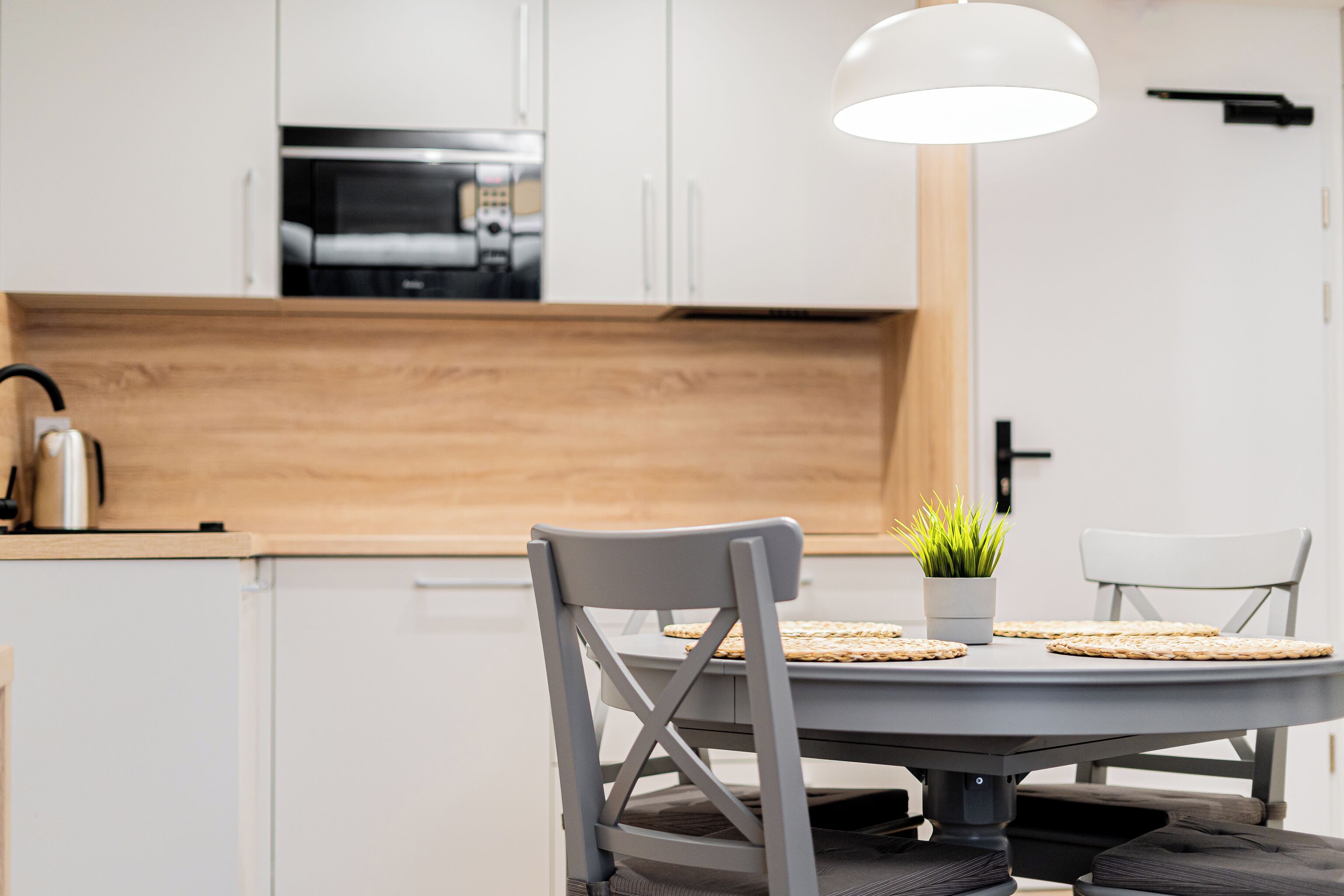 A modern kitchen with white cabinets, a wooden countertop, and a round dining table with two chairs.