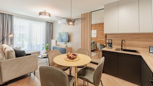 A modern living room with a sofa, a dining table with chairs, a kitchen area with a sink, and a TV on the wall. - Apartments & SPA Posesja Plażowa Grzybowo by POSESJA APARTAMENTY 4a I (Grzybowo)