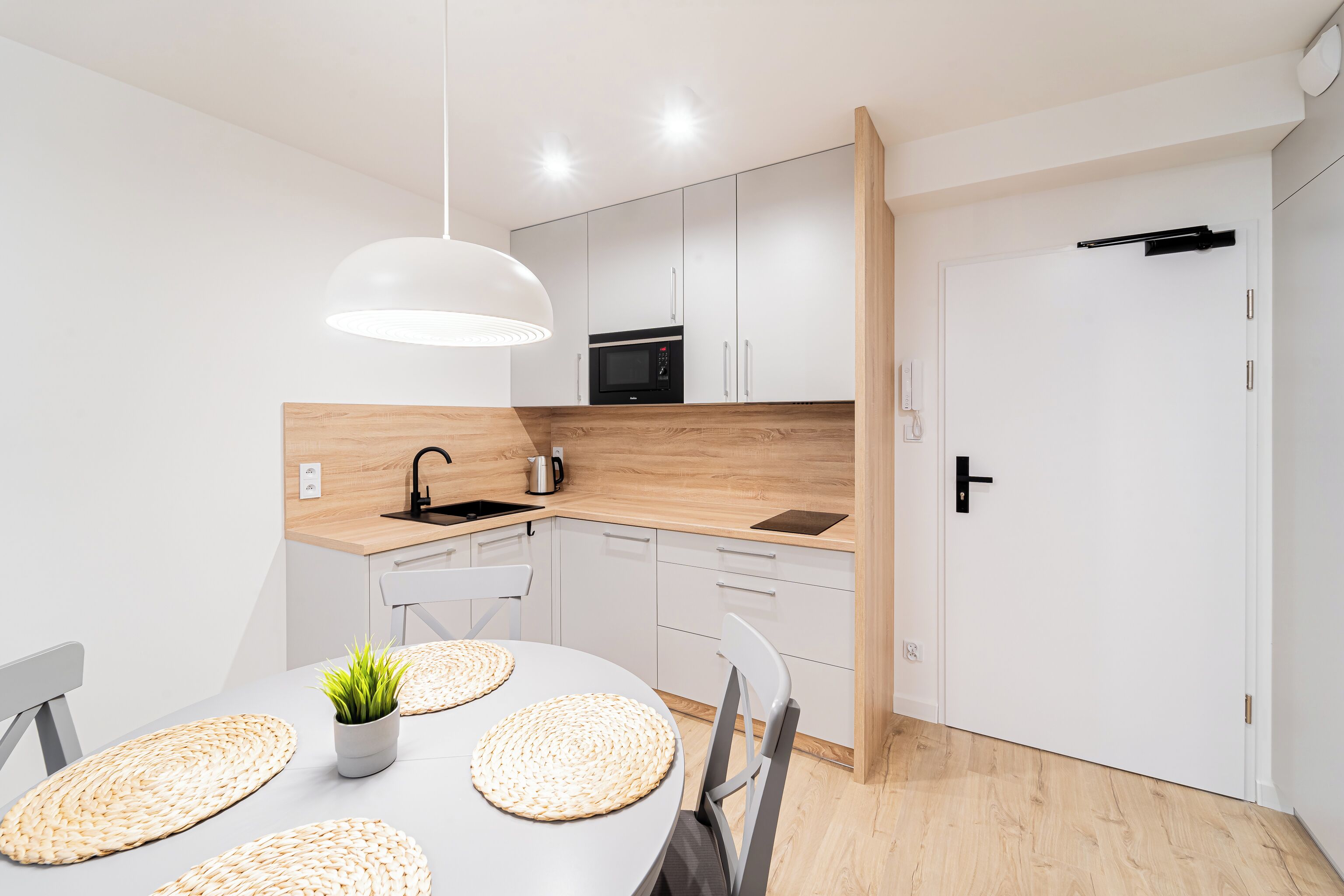 Une cuisine moderne avec des meubles blancs, un four à micro-ondes et un évier. On y trouve une table à manger avec des sets de table et une plante.