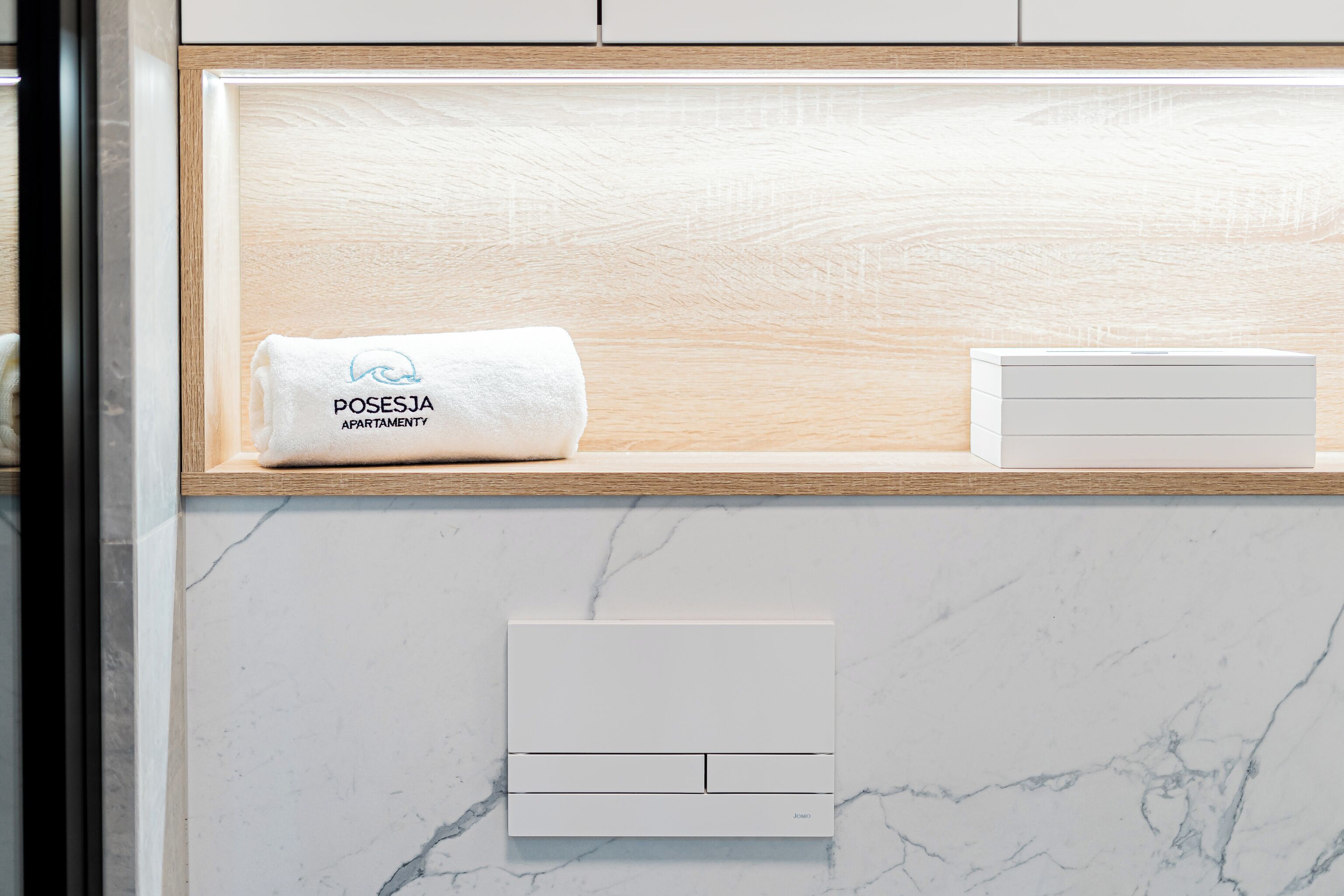 Een badkamer met een marmeren wand, een handdoek met het logo 'POSESJA APARTMENT' en een witte handdoekwarmer.