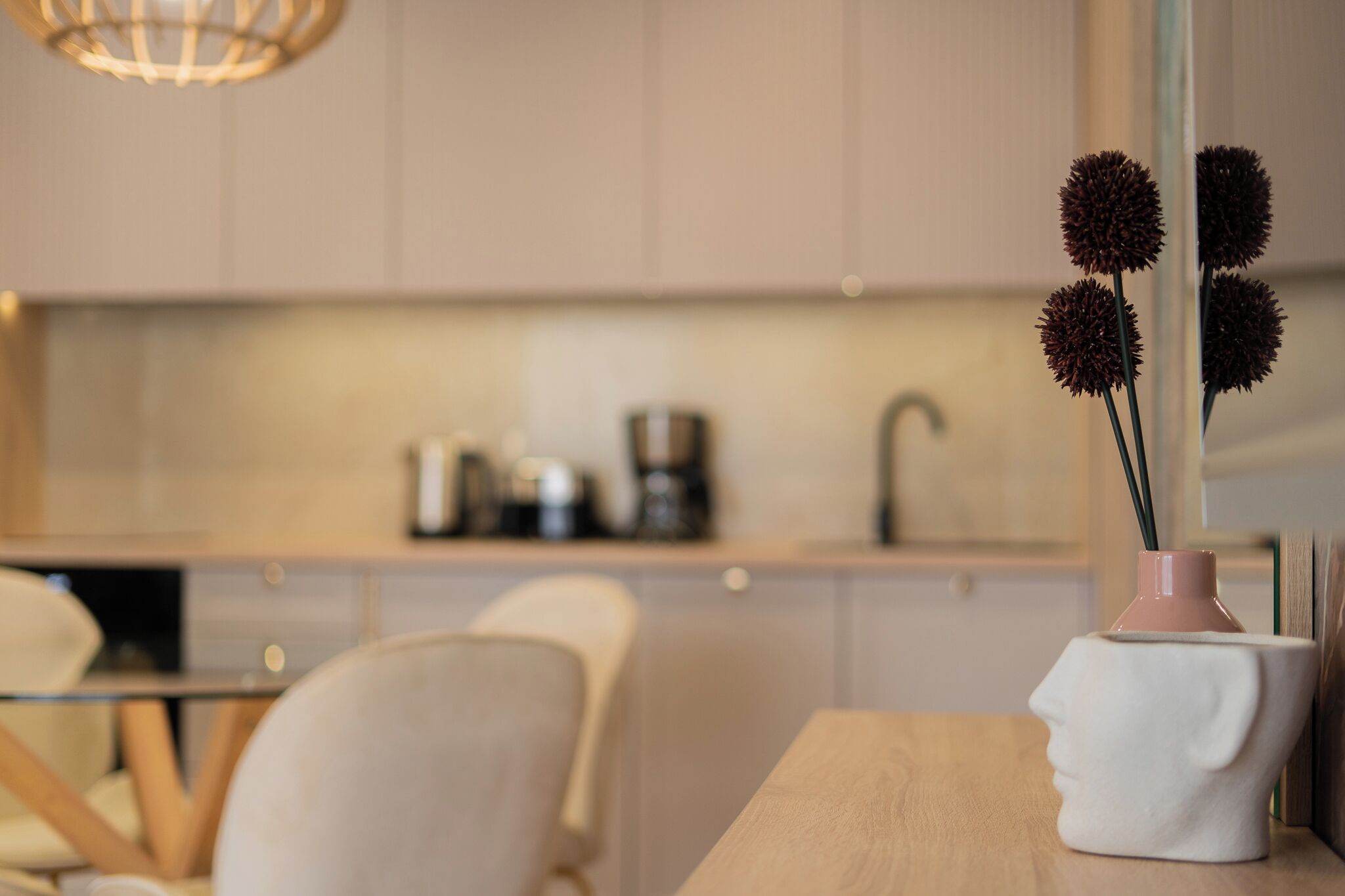 Une cuisine moderne avec un coin repas, une machine à café et un vase contenant des fleurs séchées, posé sur une table.