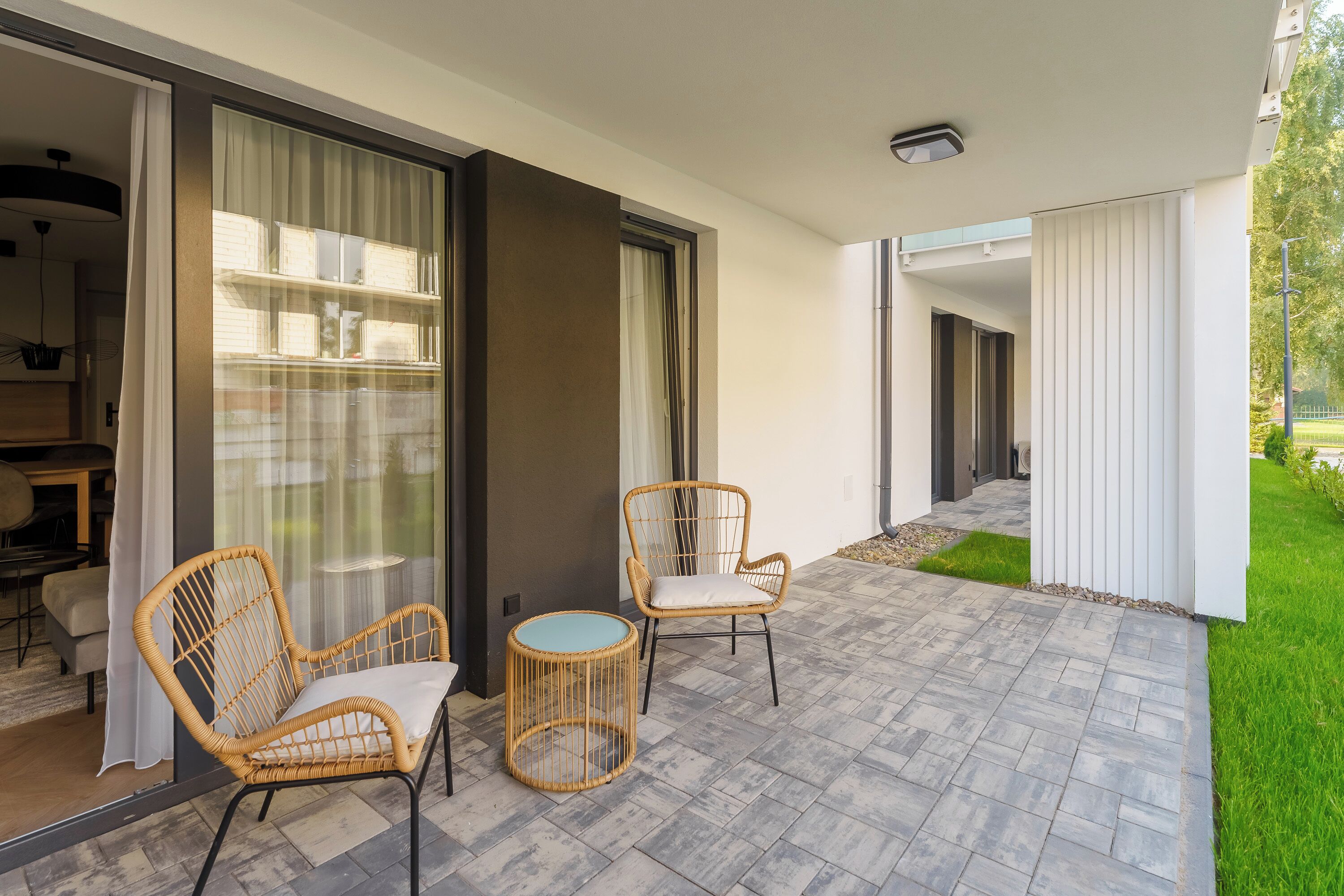 Un espace extérieur moderne aménagé avec des chaises en osier et une table ronde, une porte vitrée donnant sur une pièce, et une terrasse dallée.