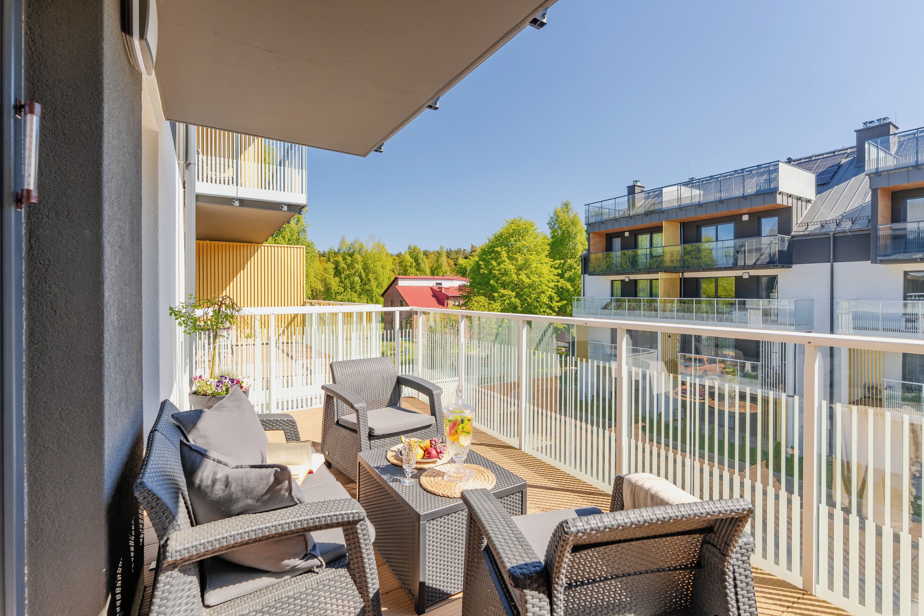 Ein Balkon mit Korbmöbeln, einem Tisch mit einem Getränk und Blick auf benachbarte Gebäude.