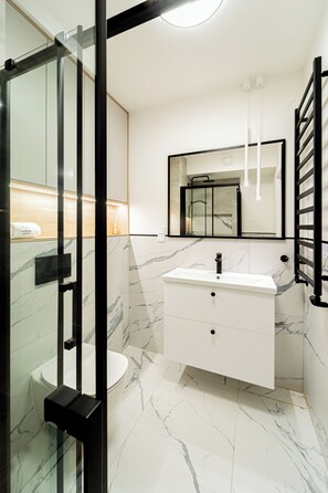 A modern bathroom with a glass shower enclosure, a white vanity with a marble countertop, and a large mirror above the sink. - Apartments & SPA Posesja Plażowa Grzybowo by POSESJA APARTAMENTY 4a I (Grzybowo)