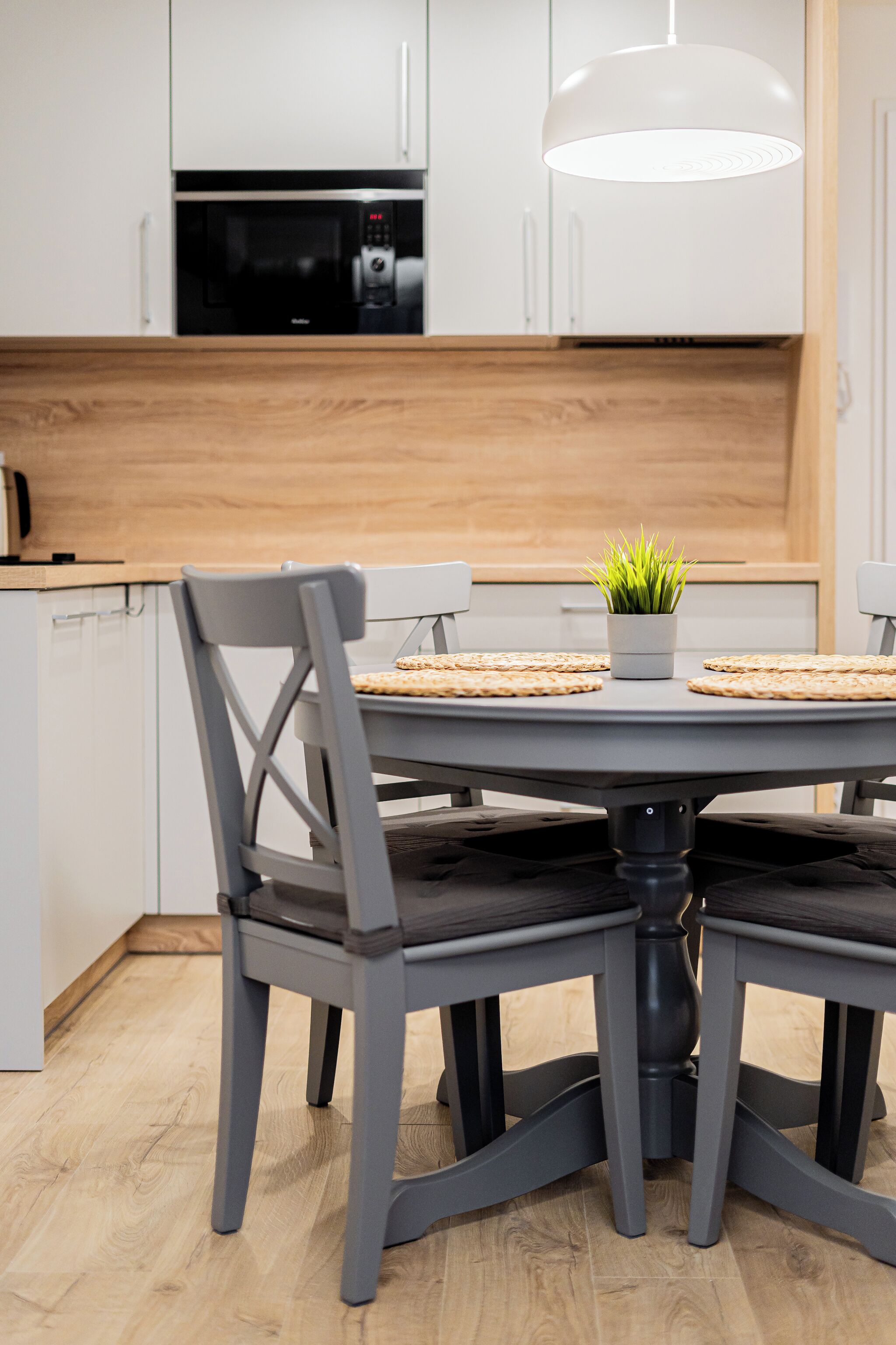 Cozinha moderna com armários brancos, micro-ondas preto e uma mesa de jantar redonda com quatro cadeiras.