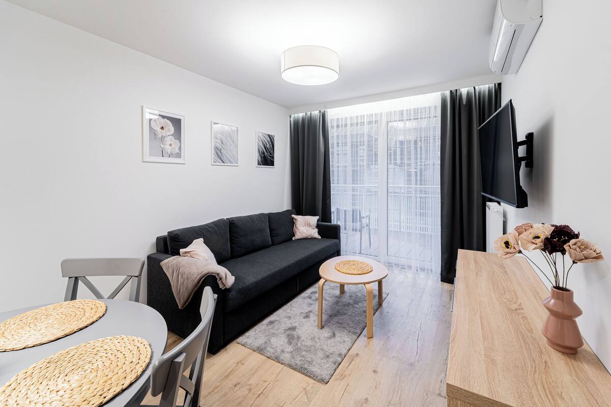 A modern living room with a grey sofa, a round wooden table, and a grey rug.