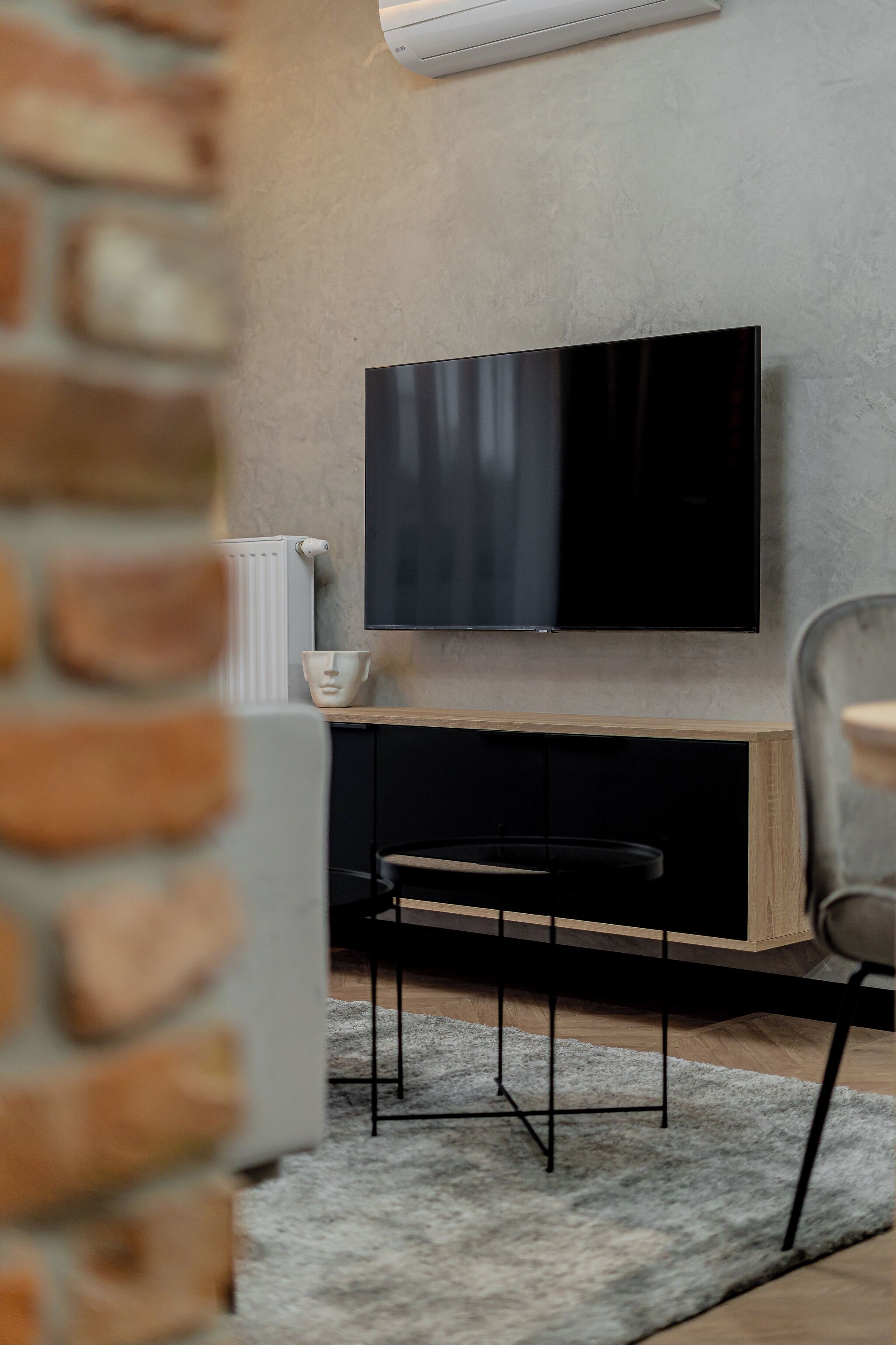 Un salon moderne avec un téléviseur à écran plat fixé à un mur texturé, un meuble en bois en dessous et un tapis gris sur le sol.