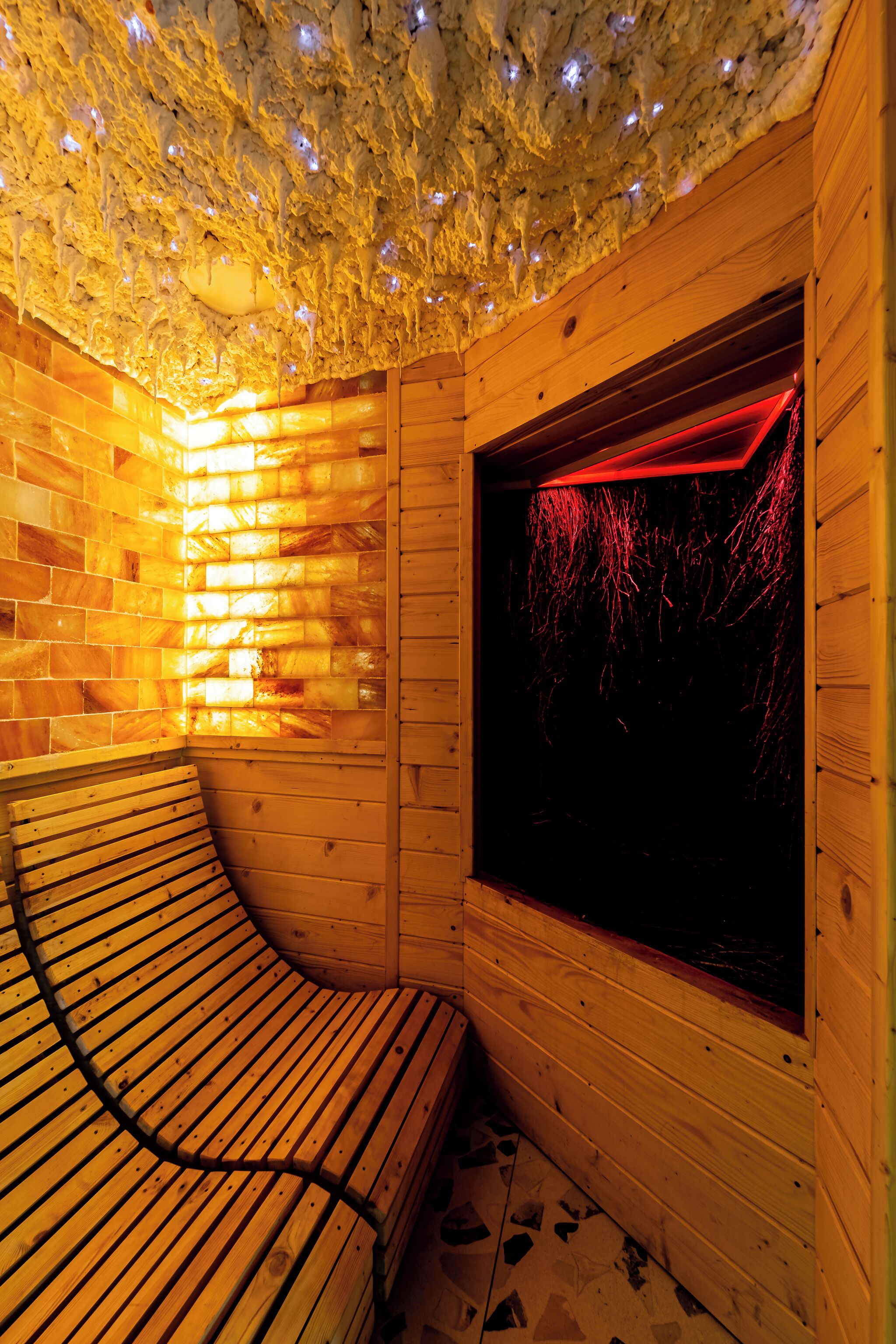 A sauna with wooden walls, a bench, and a window with red lighting.