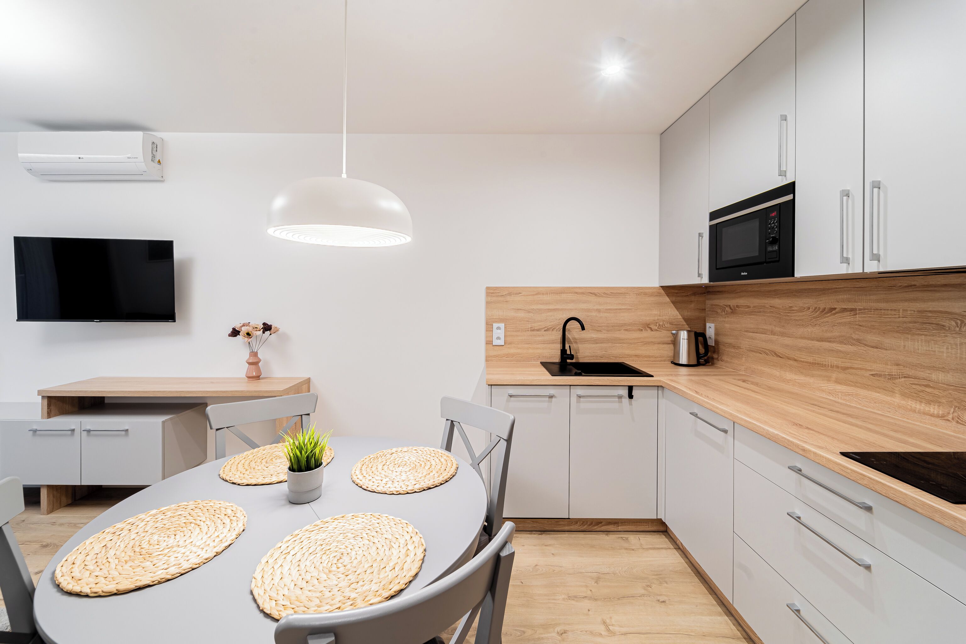 A modern kitchen with a dining area, featuring a flat-screen TV, a microwave, and a wooden countertop.