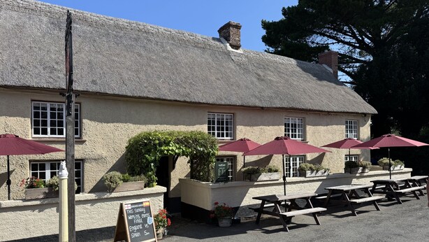 A building with a thatched roof, outdoor seating with umbrellas, and a signboard.