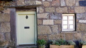 A stone building with a light-colored door, a small window, and potted plants on the ground.