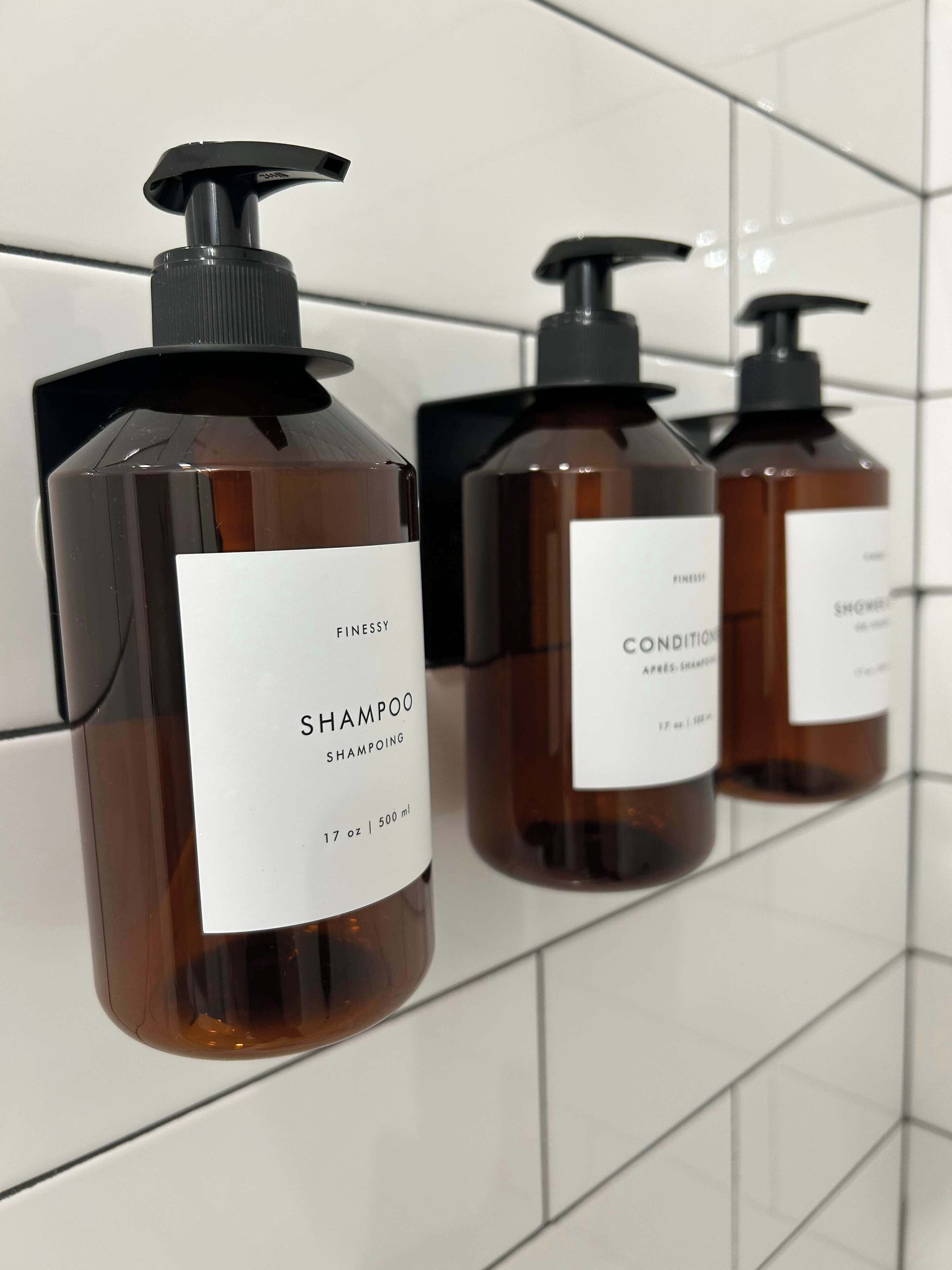 Drei Flaschen Finessy Shampoo und Conditioner auf einer gefliesten Wand.