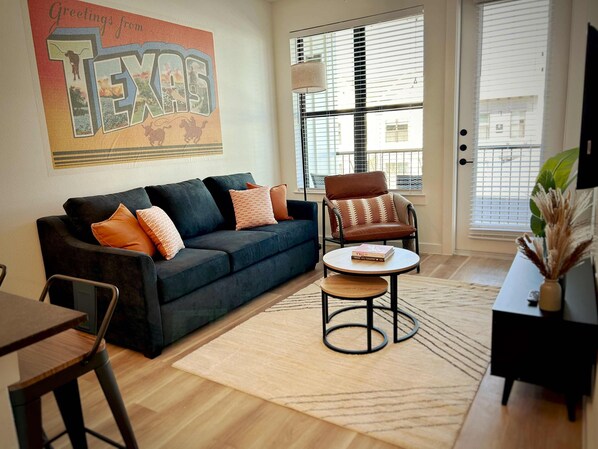 A living room with a dark blue sofa, a brown leather chair, a round coffee table, and a large wall decoration of Texas.