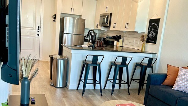 A modern kitchen with stainless steel appliances, a bar area with stools, and a dining area with a table and chairs. - Charming 1BR Retreat - Walk to Gruene Hall + Upscale Amenities (New Braunfels)