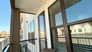 A balcony with a wicker chair and a table, large windows with blinds, and string lights. - Charming 1BR Retreat - Walk to Gruene Hall + Upscale Amenities (New Braunfels)