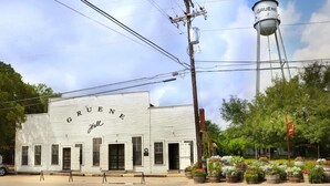 A white building with "GRUENE Hall" written on it, a water tower in the background, and a flower garden in front. - Charming 1BR Retreat - Walk to Gruene Hall + Upscale Amenities (New Braunfels)