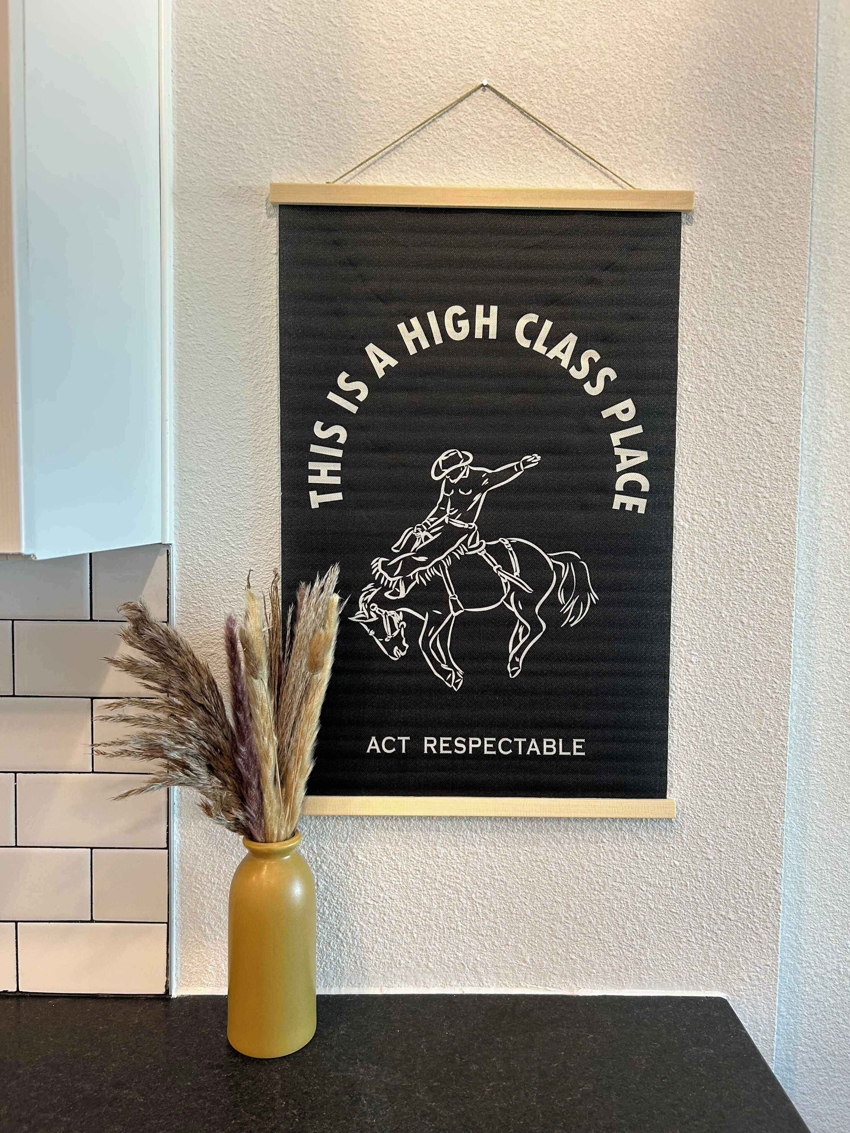 Een lijst met een poster waarop een cowboy te paard rijdt, tekst en een vaas met gedroogde planten.