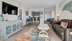 Un salon moderne avec un téléviseur, un coin repas avec des chaises, un canapé et une table basse.