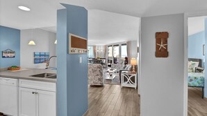 A modern kitchen with a built-in dishwasher, a dining area with a table and chairs, and a living room with a sofa and a coffee table. - Serene Oceanfront 3 bedroom condo with breathtaking views (North Topsail Beach)