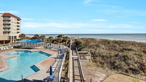 A beachfront hotel with a swimming pool, lounge chairs, and a wooden deck overlooking the ocean. - Serene Oceanfront 3 bedroom condo with breathtaking views (North Topsail Beach)