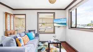 A living room with a grey sofa, colorful cushions, a black coffee table, and a large window with a beach view. - Lionel Gem – walk to Shoal Bay beaches and shops (Shoal Bay)
