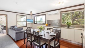 A modern kitchen with a dining area, a built-in oven, and a large window offering a view of trees. - Lionel Gem – walk to Shoal Bay beaches and shops (Shoal Bay)