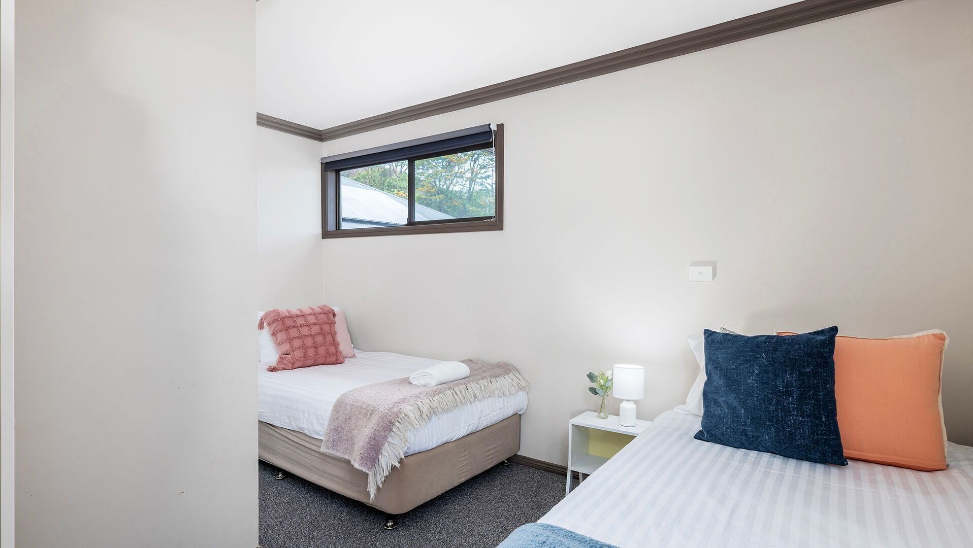 Een slaapkamer met twee bedden, een raam, een nachtkastje en een lamp.