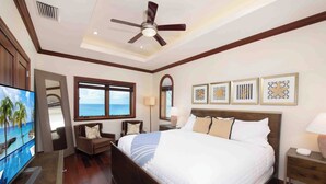 A hotel room with a large bed, a ceiling fan, a TV, and a view of the ocean.