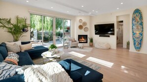A modern living room with a sofa, coffee table, fireplace, and a TV mounted on the wall. - Surf Loft just blocks from Pleasure Point! (Pleasure Point)