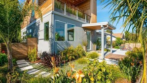 A modern two-story house with a balcony, surrounded by a well-maintained garden with various plants and a wooden deck. - Surf Loft just blocks from Pleasure Point! (Pleasure Point)