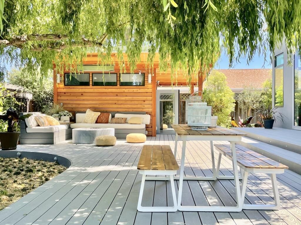 Eine Holzterrasse mit Gartenmöbeln, einer Sitzecke und Blick auf ein modernes Gebäude.