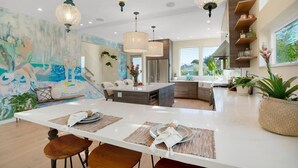 A modern kitchen with a central island, pendant lighting, and a mural on the wall. - Surf Loft just blocks from Pleasure Point! (Pleasure Point)