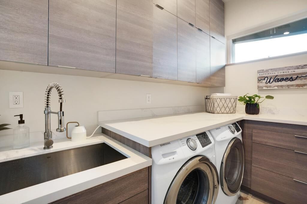 A modern kitchen with a stainless steel sink, a washing machine, and wooden cabinets.
