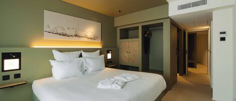 Una habitación de hotel moderna con una cama grande, mesitas de noche, una obra de arte en la pared y un vestidor.