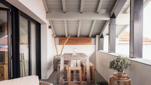 Een balkon met een houten tafel en stoelen, een bloempot en een rieten mand.