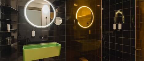 Un baño moderno con un lavamanos verde, dos espejos redondos y una ducha con cerramiento de vidrio.