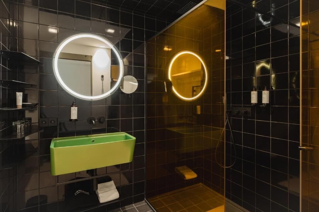 Een moderne badkamer met een groene wastafel, twee ronde spiegels en een douchecabine met glazen wanden.