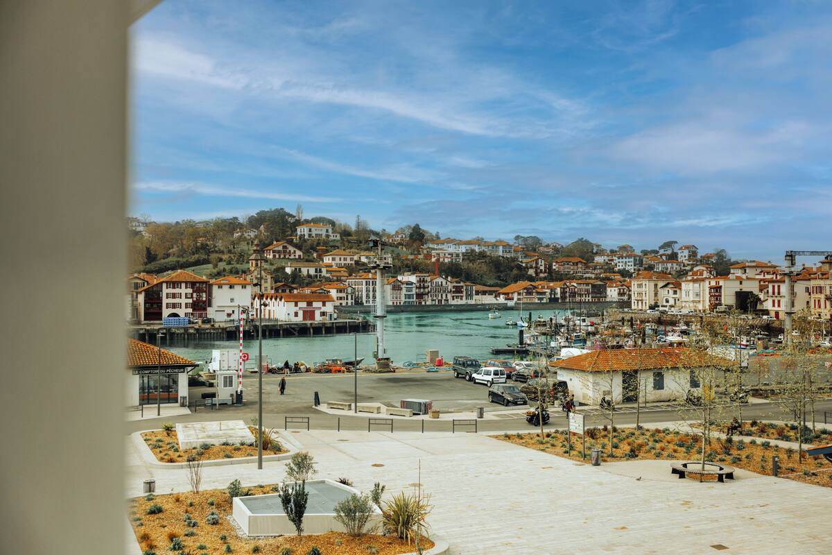 Un pueblo costero con un puerto deportivo, edificios con tejados anaranjados y un cielo despejado.